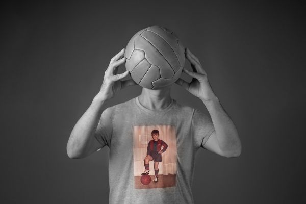 Imatge en blanc i negre d'un home amb una pilota de futbol antiga tapanat-li la cara