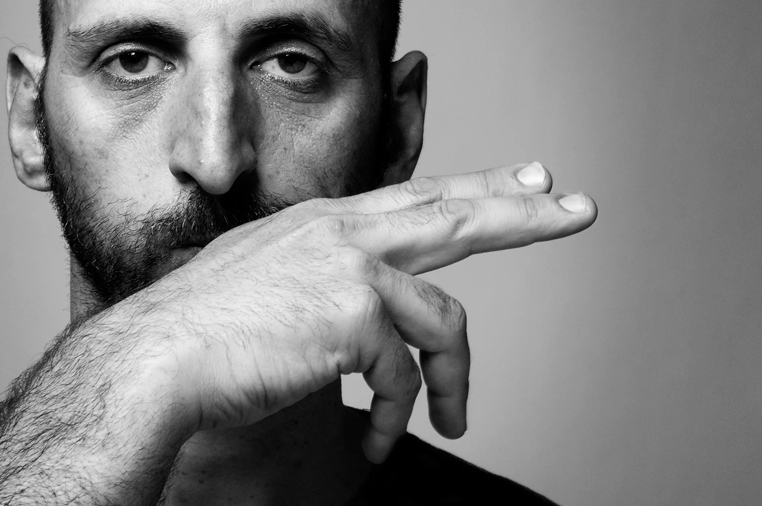 El actor Toni Gomila en primer plano haciendo el símbolo de unas tijeras con la mano tapándose la parte inferior de la cara