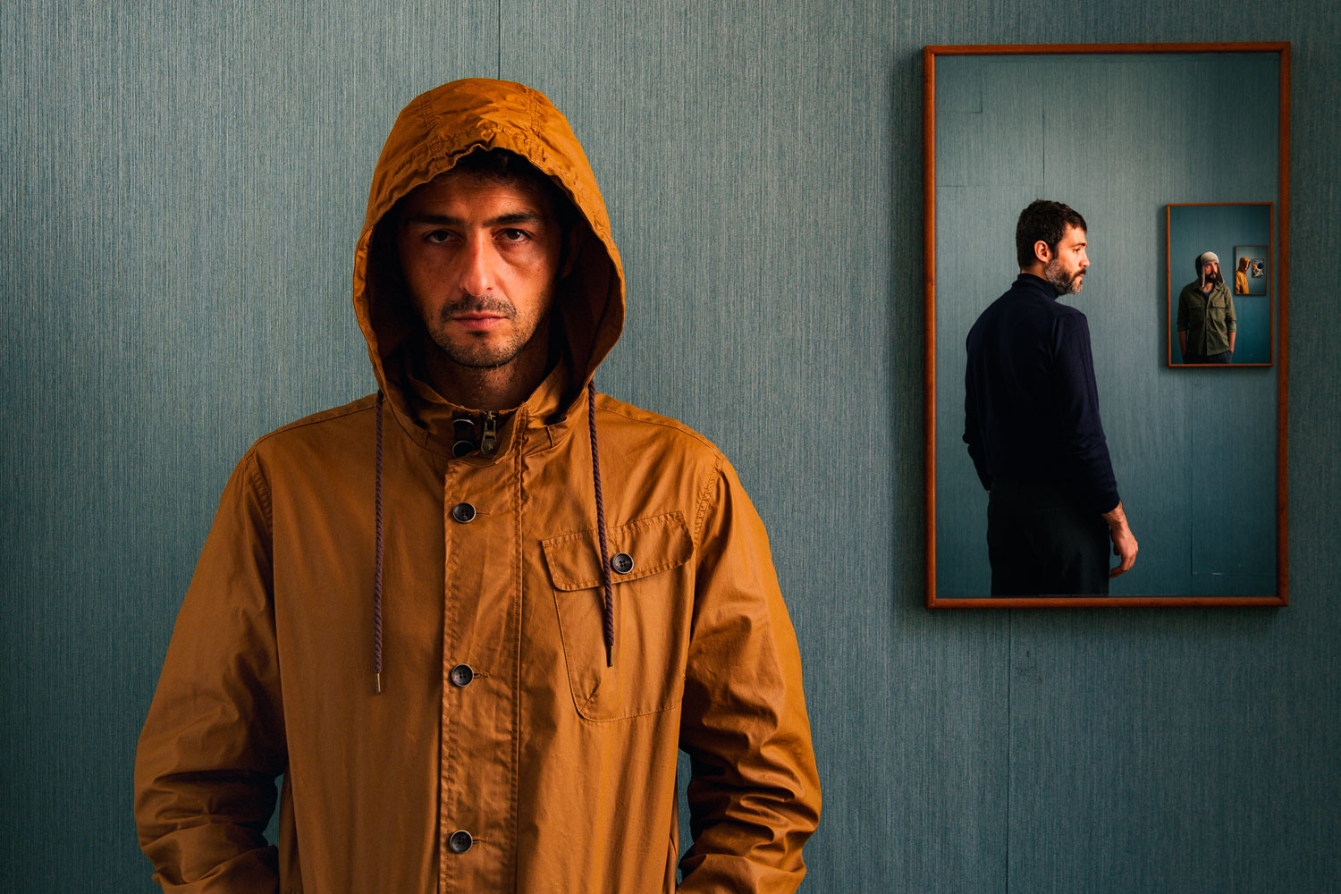 Fotografia de mig cos d'un noi amb jaqueta marró i caputxa, la qual porta posada. Al costat dret i té un quadre amb la fotografia d'una noi d'esquena, vestit de negre, el qual a la vegada té un quadre a l'esquerra amb la fotografia d'una altre noi, i així successivament.