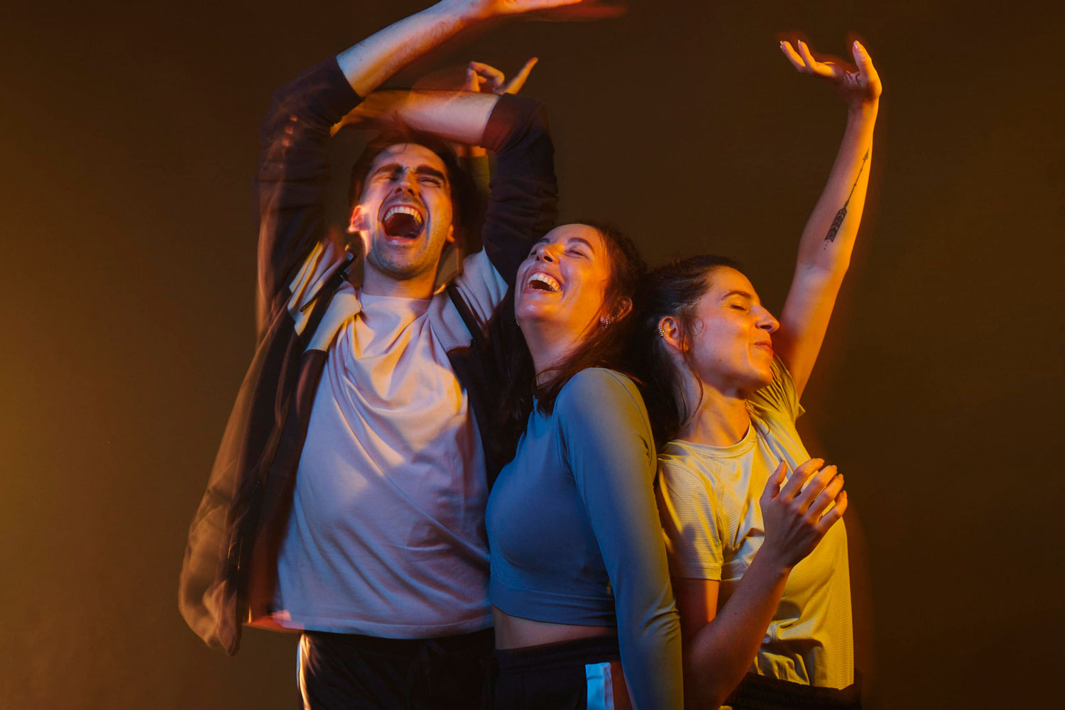 Un noi i dues noies ballant amb els braços enlaire i amb expressió de passar-ho bé