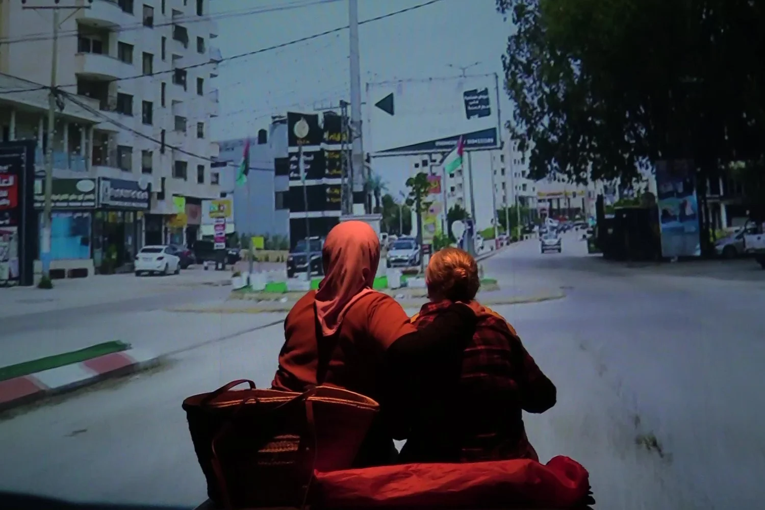 Dues dones assegudes d'esquena mirant la projecció de la imatge d'un carrer a Palestina