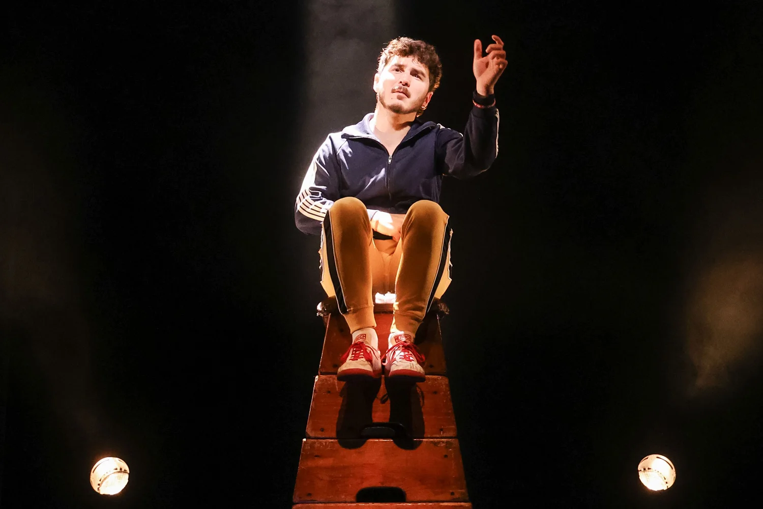 El actor Marc Balaguer sentado sobre un plíntono mirando al infinito y levantando una mano en alto