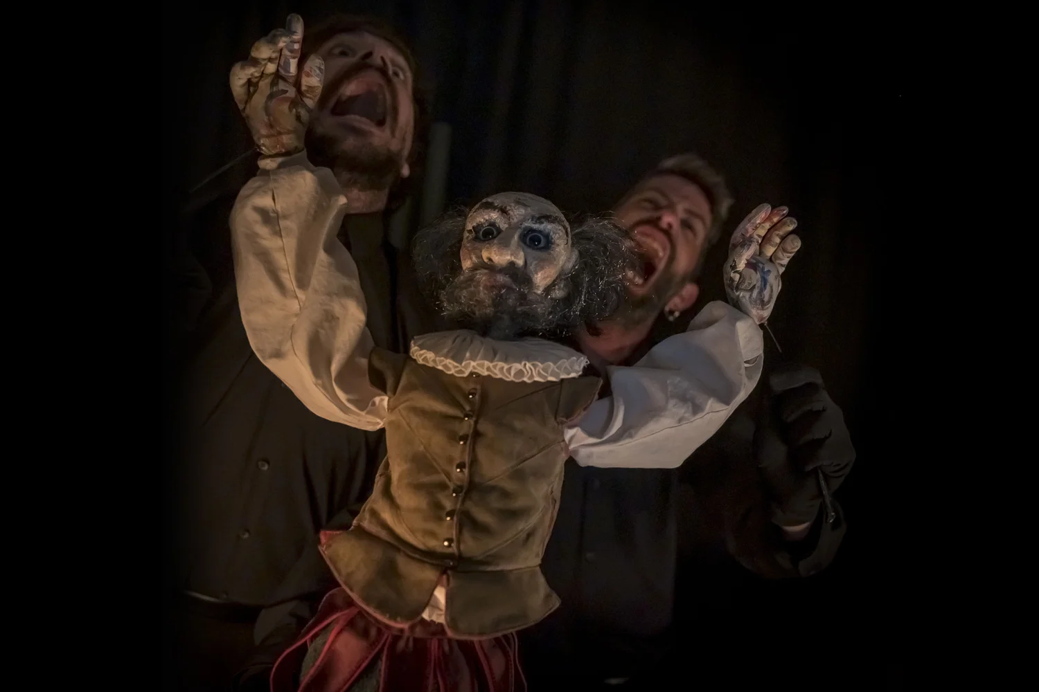 Un titella del Quixot aixcant els braços enlaire amb els dos actors i manipuladors al seu darrere cridant